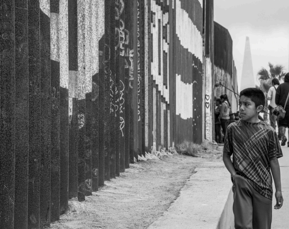 CHILD GAZES through the border wall